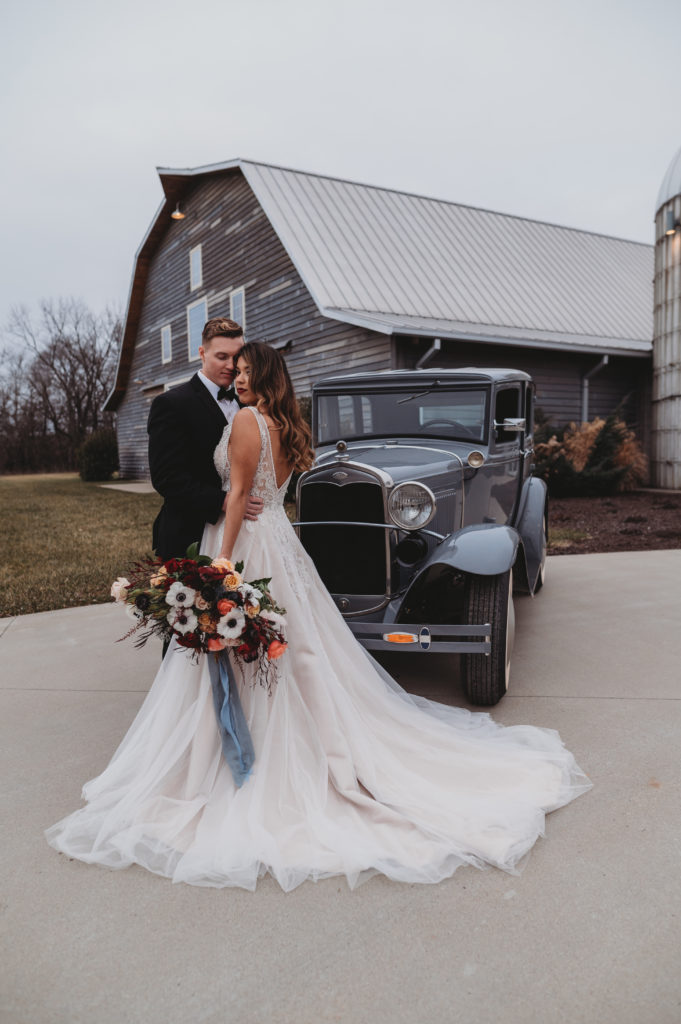 bride and groom posing in front of old car at the silo event center