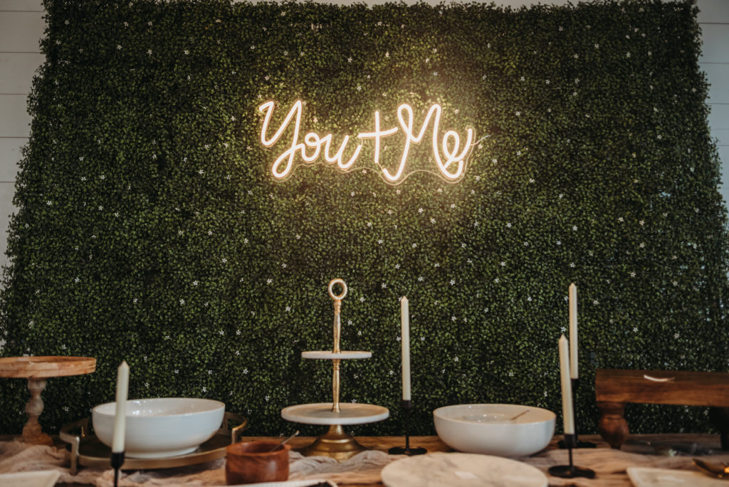 dessert table set up with greenery backdrop and 'you and me' sign behind it at barn at white oaks