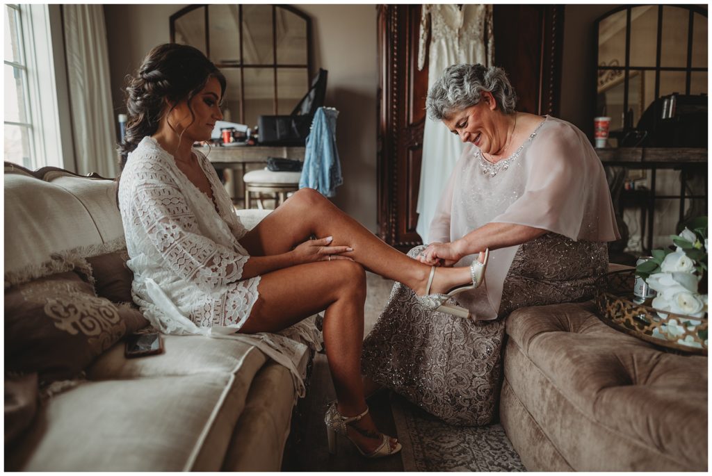 mother helping bride get shoes on for her wedding day