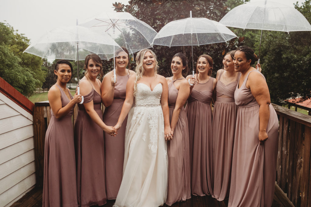 Florida bride in Vero beach with her bridesmaids in the blush dresses standing in the rain with transparent umbrellas.