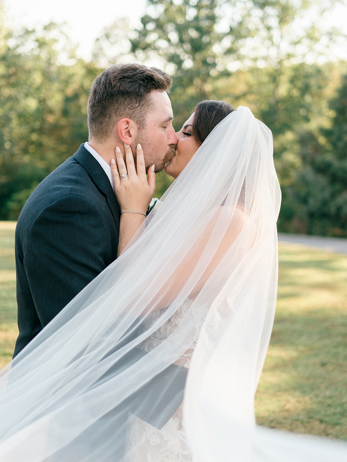 Newlyweds kiss while wrapped in a veil in a field at sunset