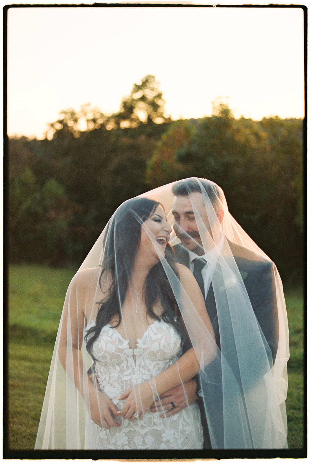 Newlyweds laugh while under a veil in a film photo from a Hybrid Wedding Photography