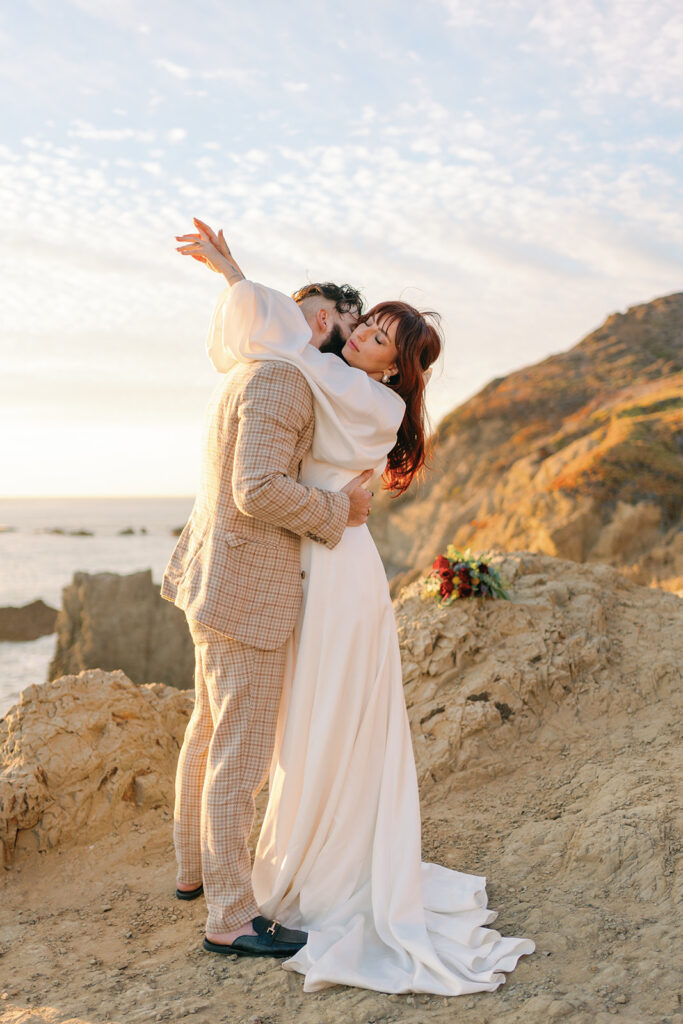Newlyweds hug at sunset on an oceanside mountain trail after using San Francisco Wedding Planners