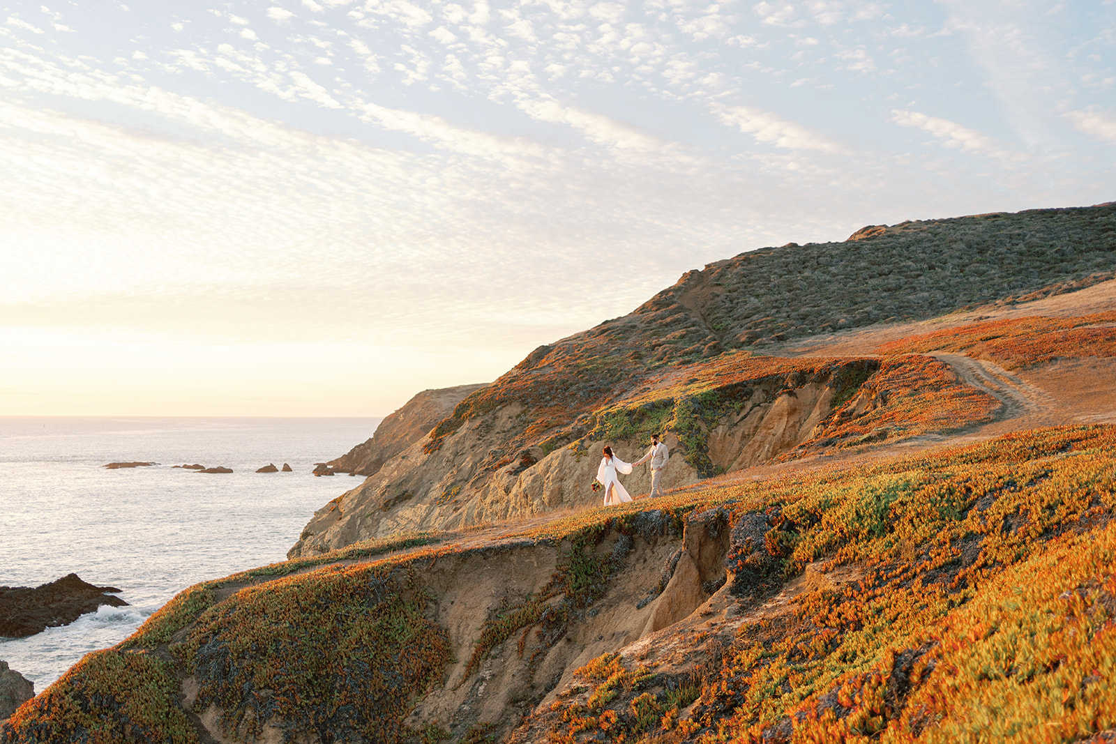 Newlyweds walk hand in hand down an oceanside trail at one of the San Francisco Wedding Venues
