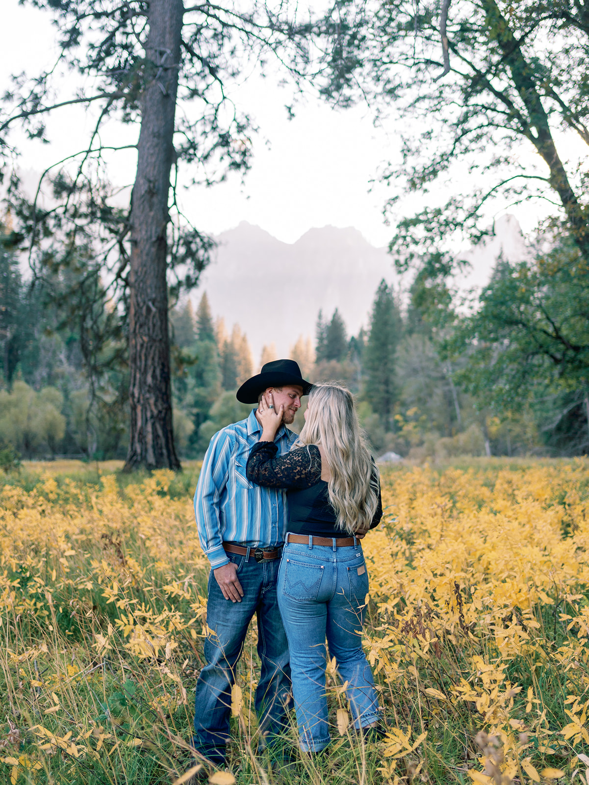 A couple share an intimate moment in jeans in a field of yellow wildflowers at a Yosemite National Park Wedding