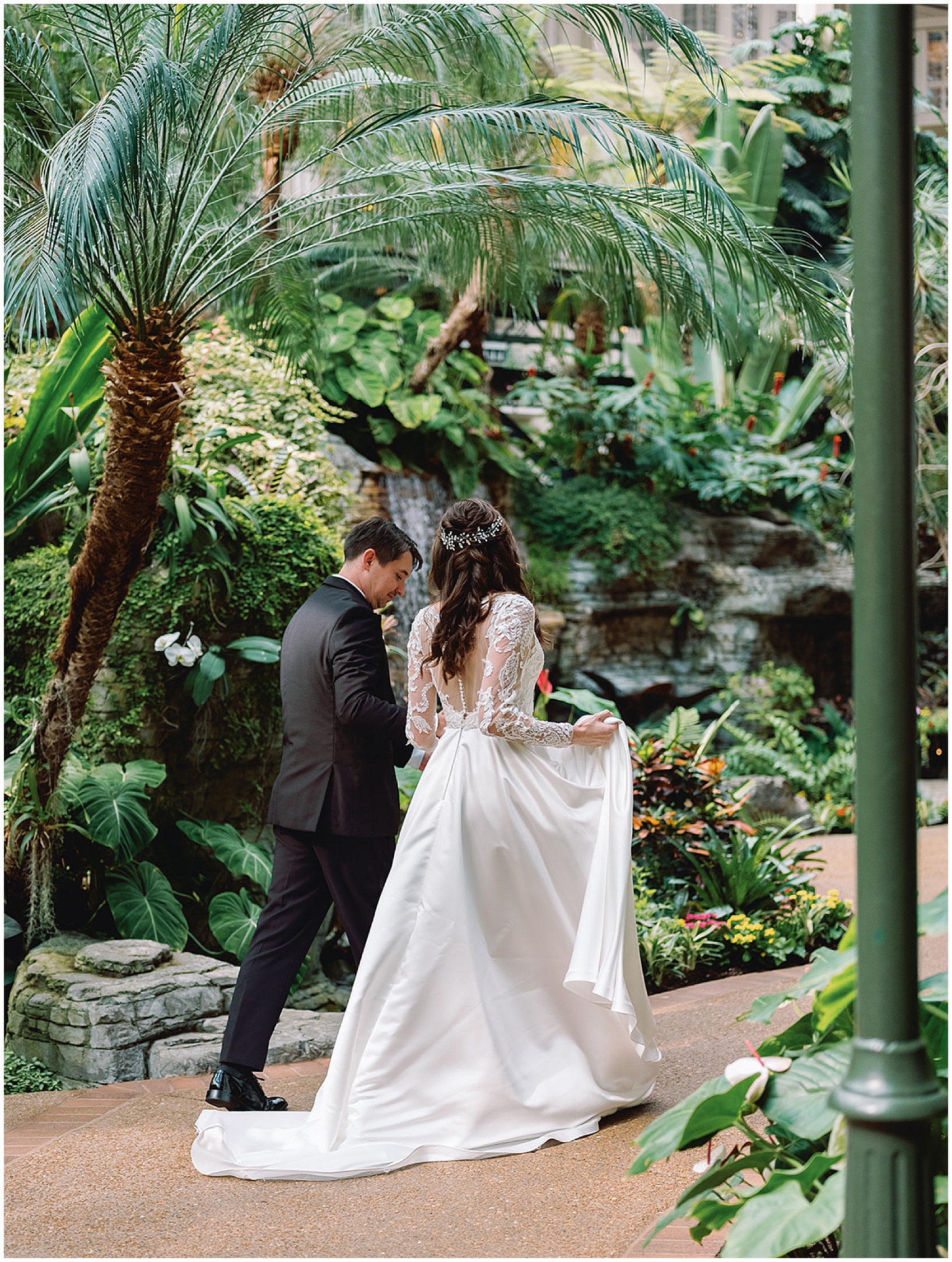 A bride and groom walk through an indoor tropical garden holding hands