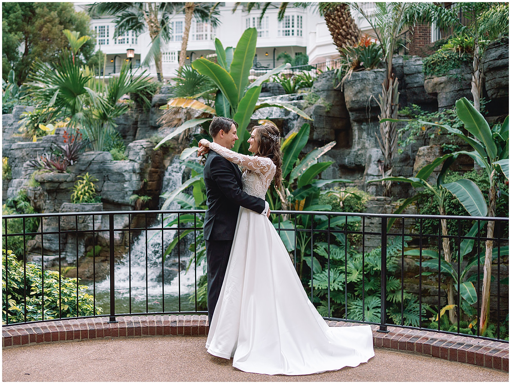Newlyweds smile at each other while hugging in a tropical garden