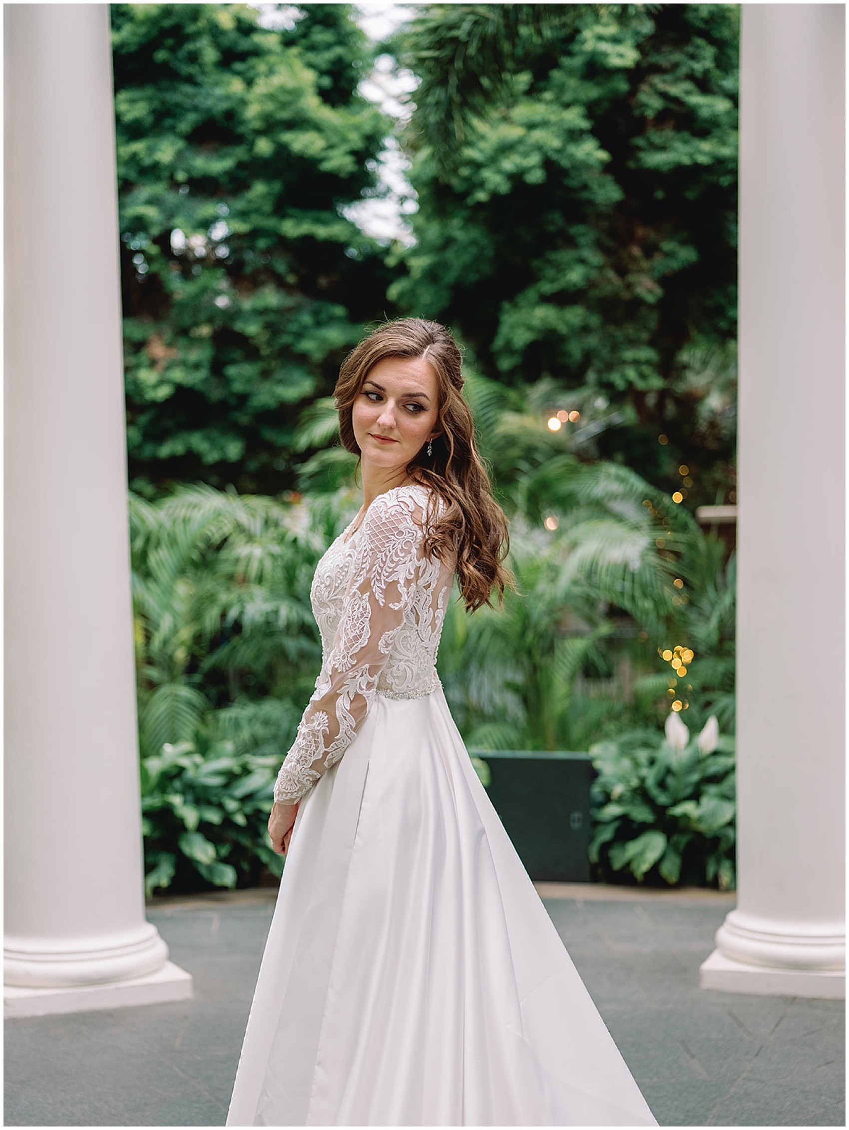 A bride looks over her shoulder in a lace embroidered dress in a garden