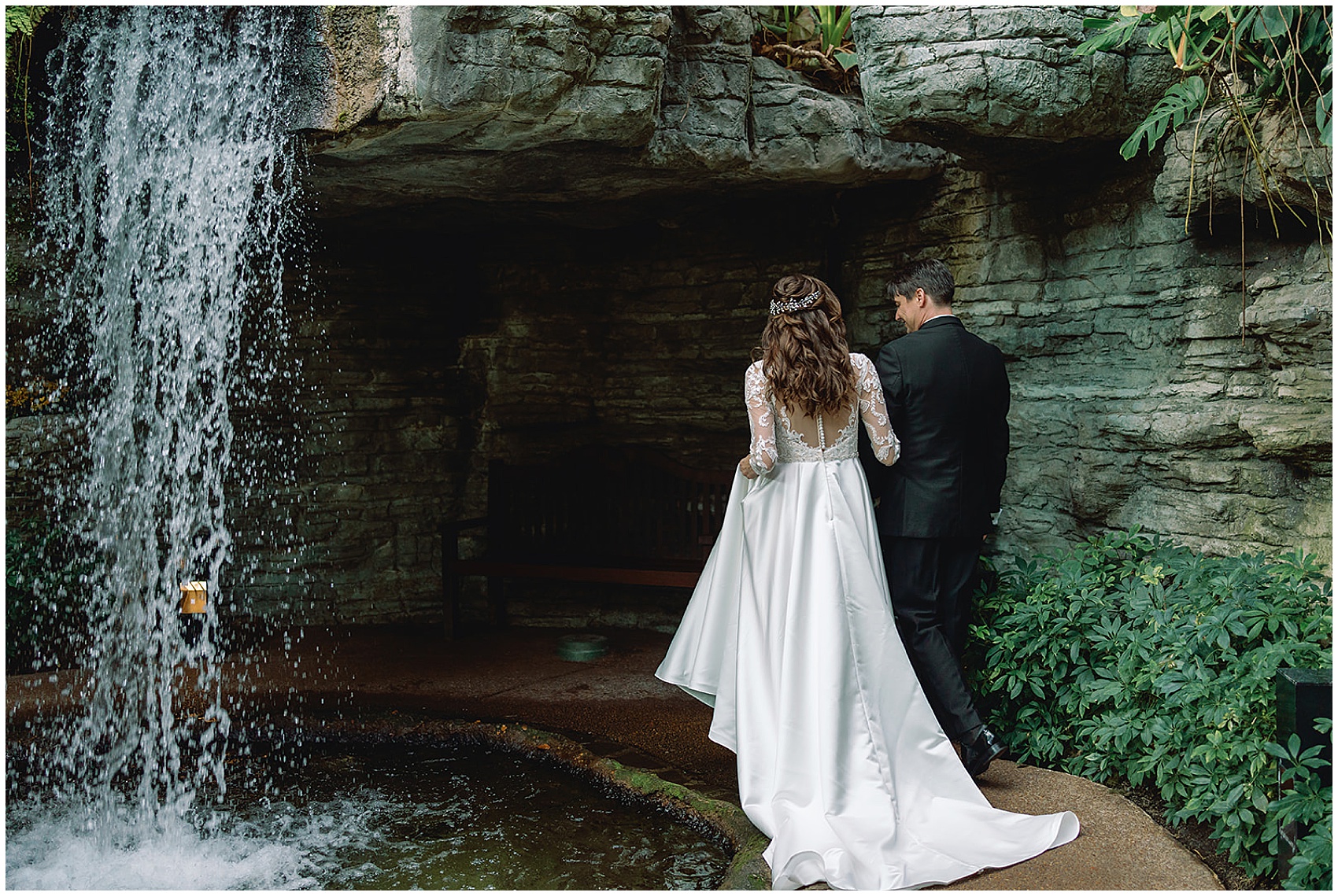 Newlyweds walk hand in hand into a cave under a waterfall at their gaylord opryland wedding
