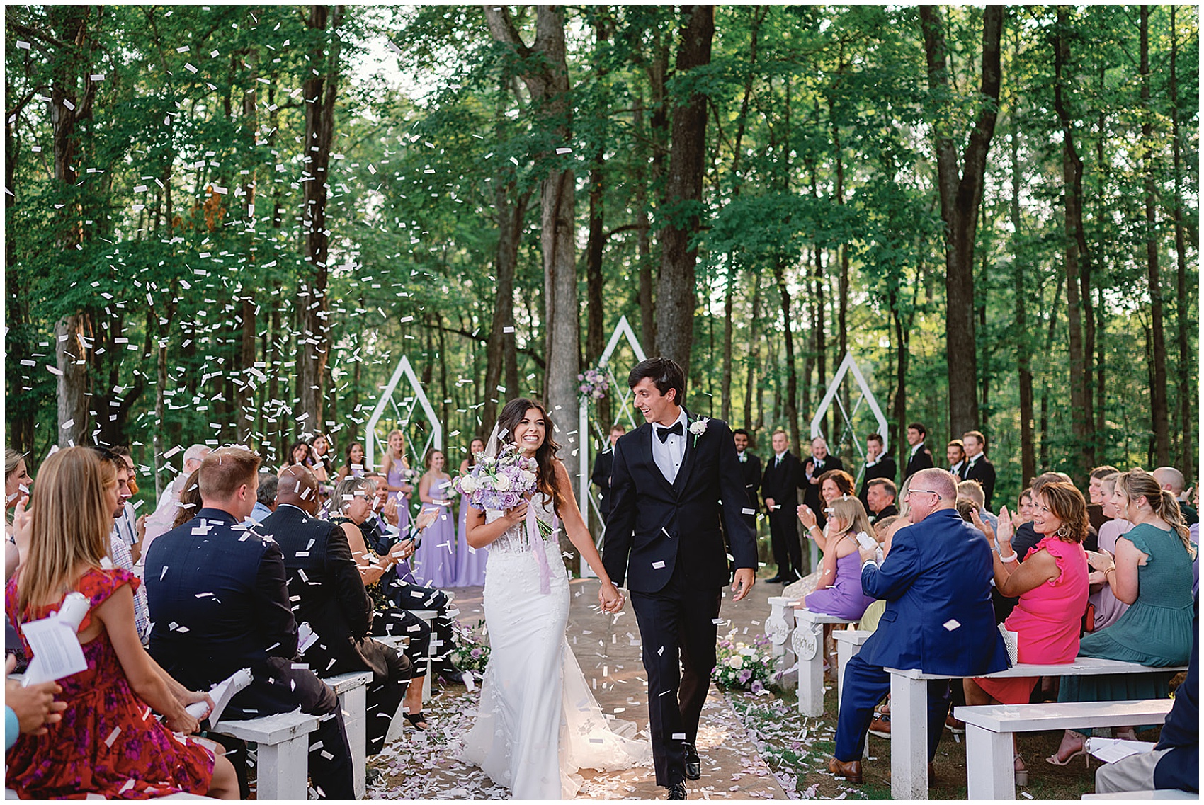 Newlyweds laugh and hold hands while walk up the aisle at their wedding reception in the woods