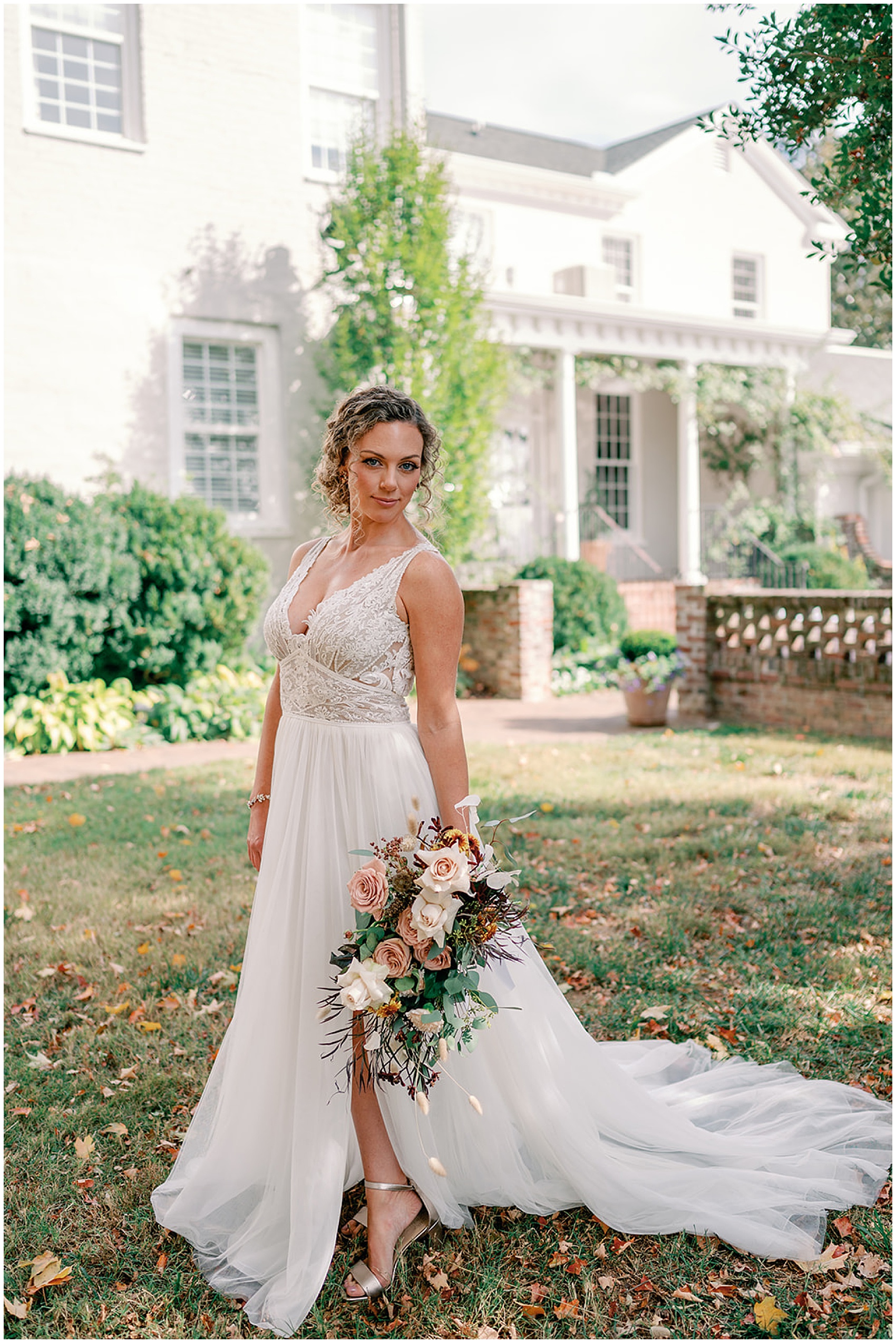 A bride stands in her lace top dress in the front garden of a wedding venue