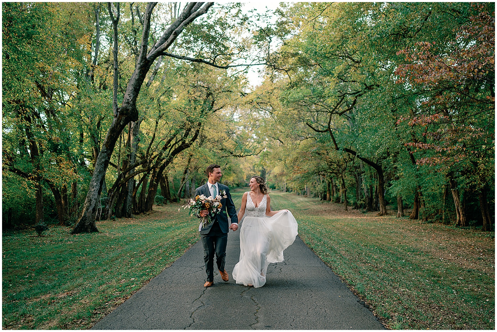 Newlyweds walk down a paved path through trees at their maple grove estate wedding