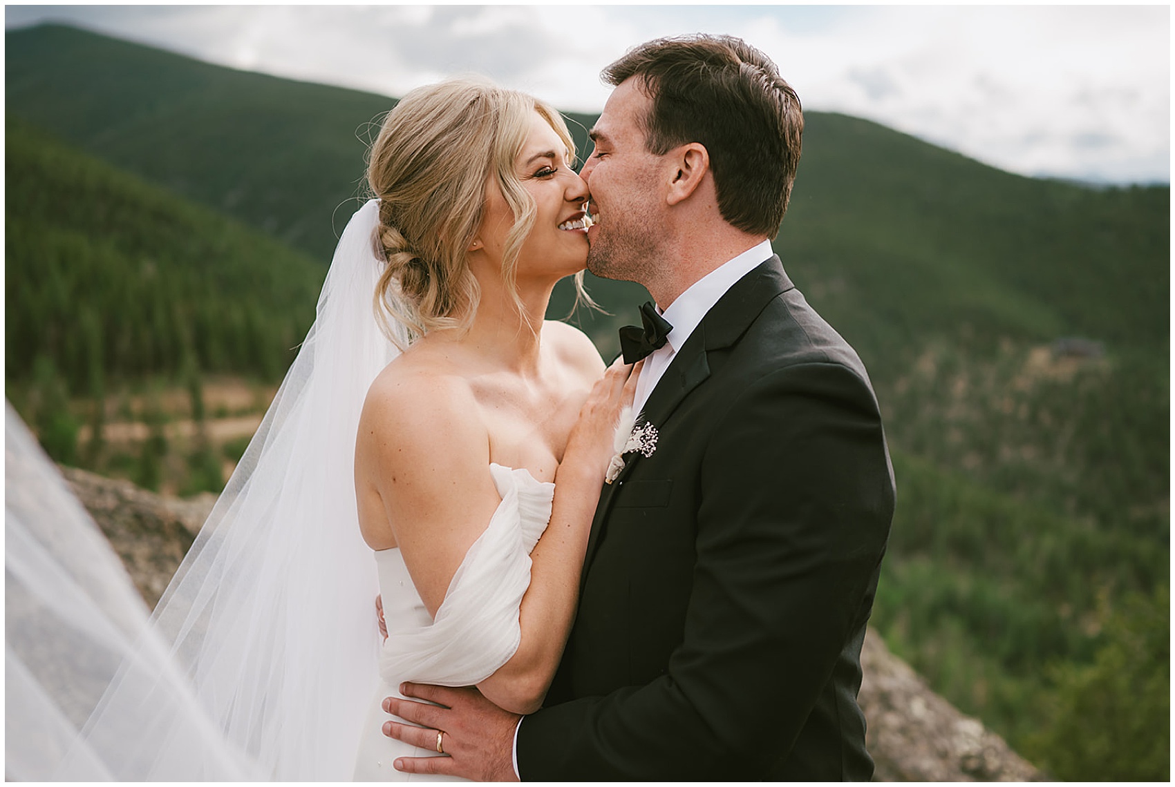 Newlyweds kiss with big smiles kiss on a mountainside trail during their north star gatherings wedding