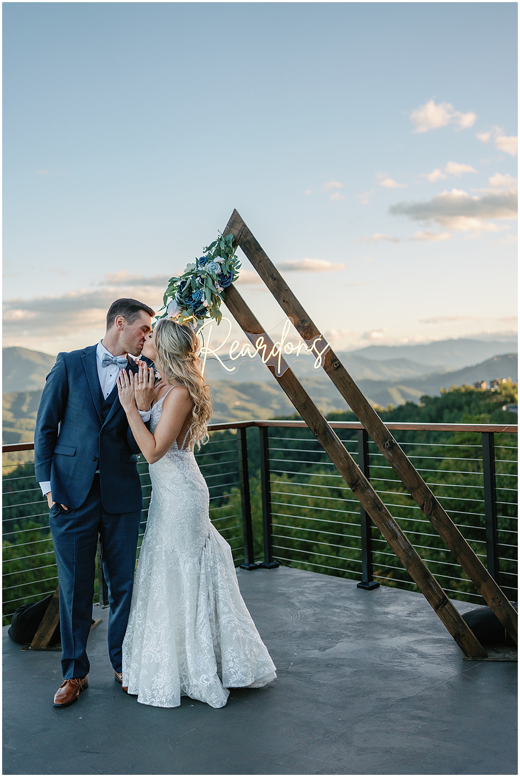 Newlyweds kiss while showing off their rings by their custom wood arbor on a mountain patio at the trillium venue