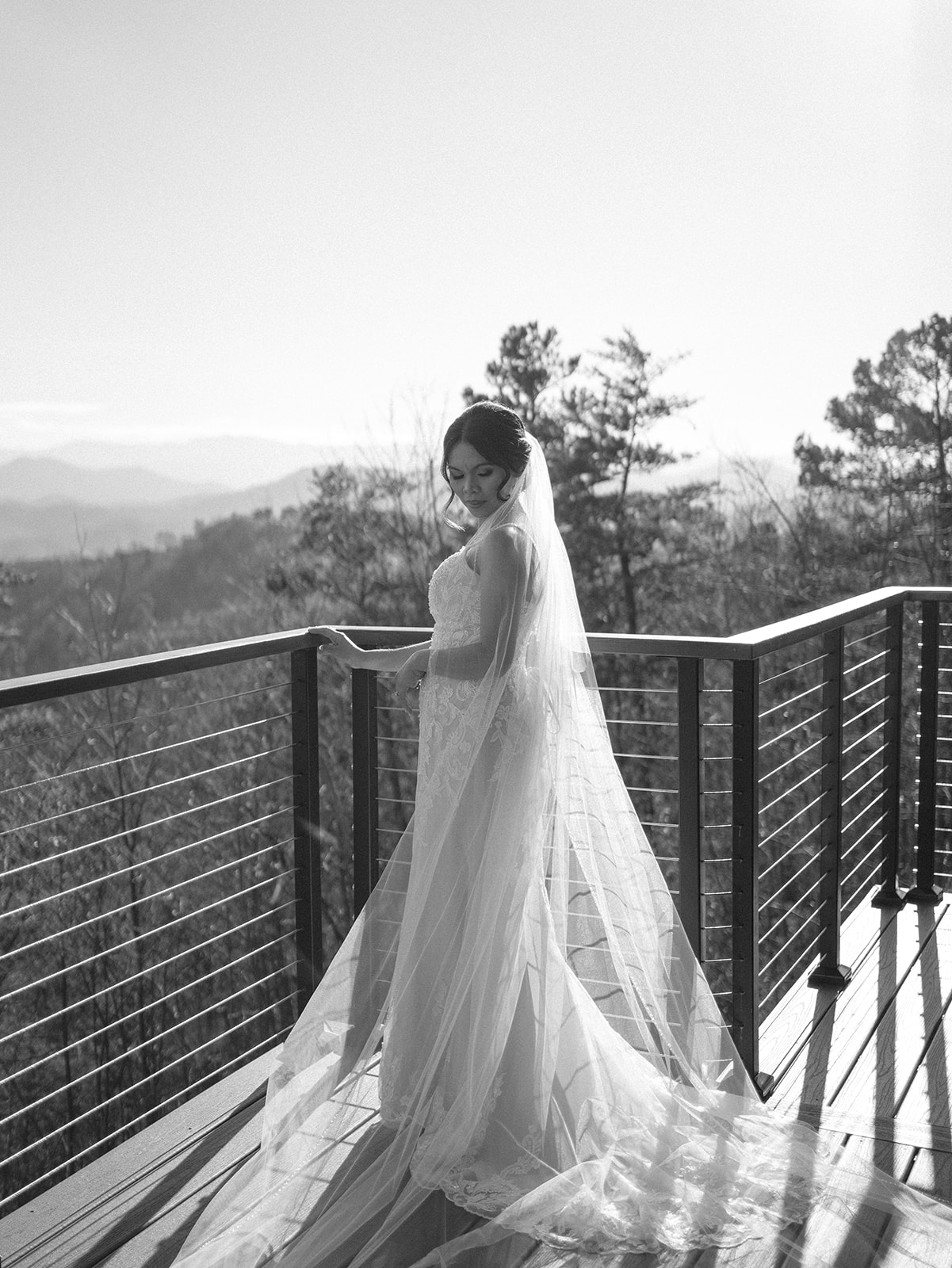 A bride stands on a mountain balcony gazing down her shoulder to her long veil behind her at her The magnolia wedding