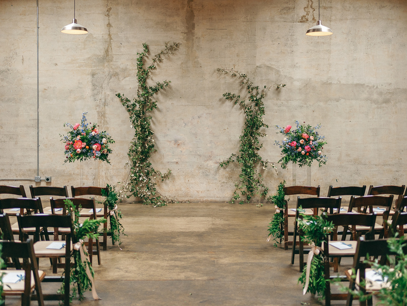 Details of a wedding ceremony set up with wooden chairs and vines on the concrete wall at The Standard Wedding Venue