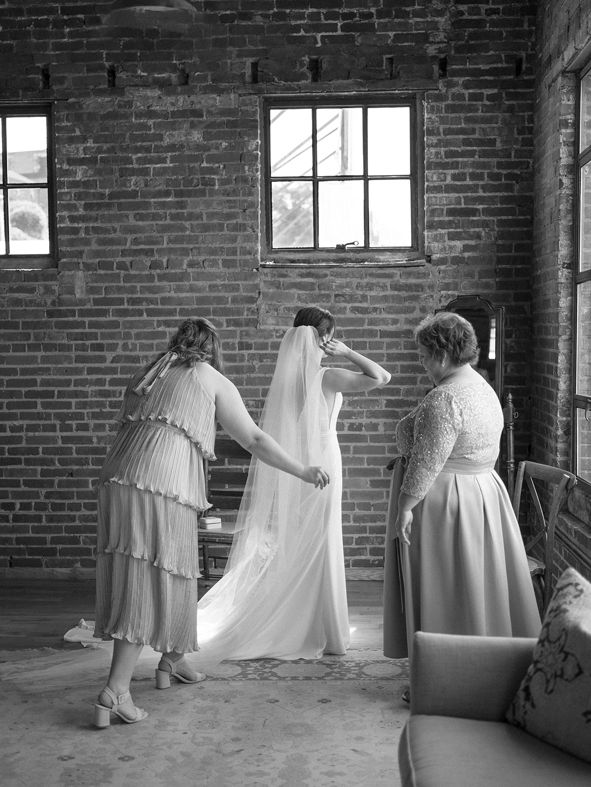 A bride gets ready with her maid of honor and mom in a mirror