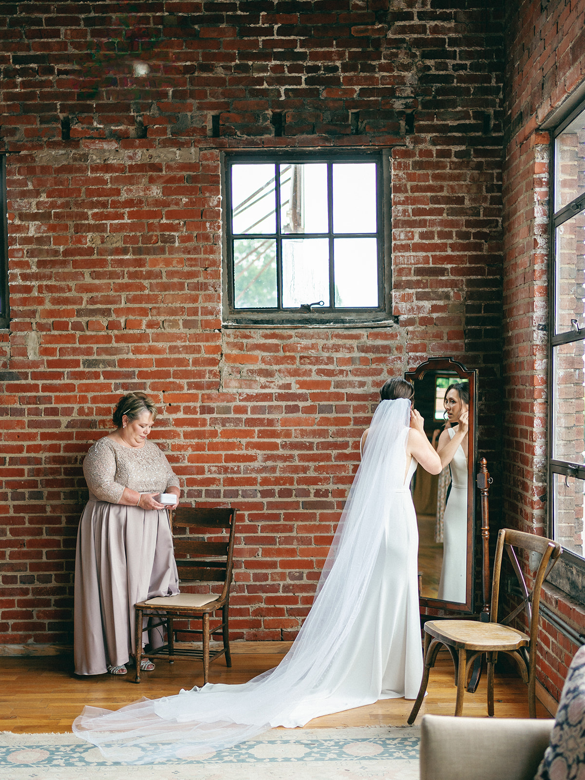 A bride puts on her earrings in a corner mirror in a brick room