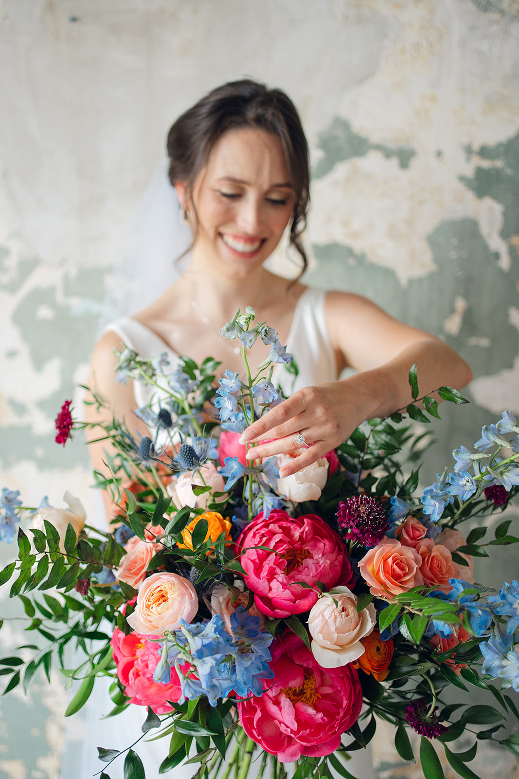 A bride smiles while showing off her colorful bright bouquet
